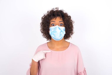 Beyaz arka planda kendini gösteren maskeli genç bir kadın. Bulaşıcı hastalıklara karşı koruma. Stüdyoda poz veren günlük kıyafetler giyen genç bir kadın.