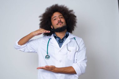  İzole edilmiş arka planda beyaz önlük giyen genç bir doktor. Ellerinde büyük ve büyük boy işareti, ölçü sembolü var. Kameraya bakıp gülümsüyor. Ölçüm konsepti.