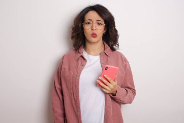 Akıllı telefonlu pembe tişört giyen genç ve güzel Latin kadın stüdyoda üzgün.