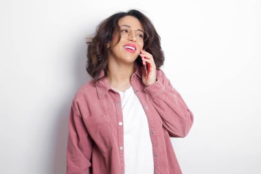 Hoş görünümlü, pembe tişörtlü, mutlu Latin bir kadın. Güzel bir telefon görüşmesi yapıyor ve yan yana bakıyor. Cep telefonuyla konuşurken güzel bir havası var ve gülümsüyor.