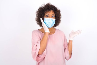 Beyaz arka planda kafası karışmış maskeli bir kadın var. Bulaşıcı hastalıklara karşı koruma. Gündelik kıyafetler giymiş genç bir kadın.