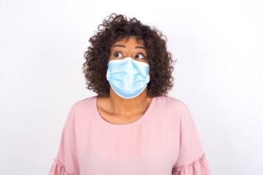 Maskeli genç bir kadın beyaz arka planda izole edilmiş. Günlük kıyafetler giymiş, yüz maskesi takan genç bir kadın. Bulaşıcı hastalıklara karşı koruma.