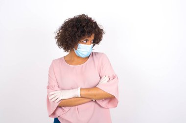 Yüzü maskeli genç bir kadın beyaz arka planda soyutlanmış bir şekilde yüzünü çeviriyor. Günlük kıyafetler giymiş, yüz maskesi takan genç bir kadın. Bulaşıcı hastalıklara karşı koruma.