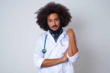 Tıbbi üniforma giyen neşeli bir doktorun, yüzü duvara yakın gri bir duvarda duruşu. İyi haberleri dinledikten sonra kameraya mutlu bir ifadeyle bakmak. Kendinden emin adam.