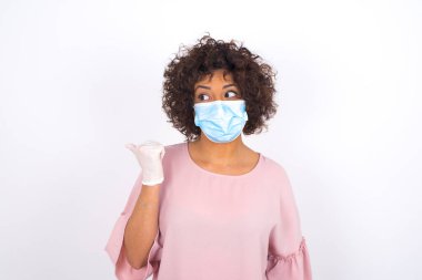 Yüzü maskeli genç bir kadın beyaz arka planda izole bir şekilde görünüyor. Bulaşıcı hastalıklara karşı koruma. Stüdyoda poz veren günlük kıyafetler giyen genç bir kadın.