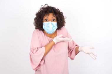 Yüz maskeli genç bir kadın beyaz arka planda izole edilmiş bir şey gösteriyor. Günlük kıyafetler giymiş, yüz maskesi takan genç bir kadın. Bulaşıcı hastalıklara karşı koruma.