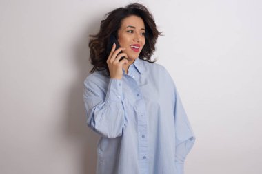 Stüdyoda mavi tişört giyen genç ve güzel bir kadın akıllı telefondan konuşuyor.