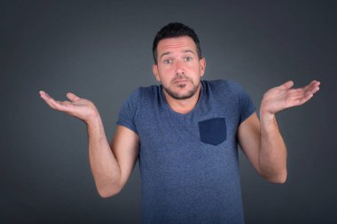 Kafası karışmış, kolları açık tişört giyen, omuzlarını silkeleyen, 