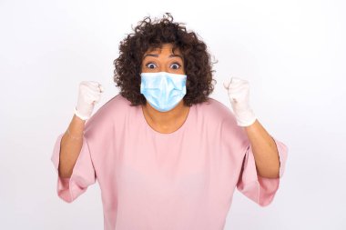 Beyaz arka planda yumrukları olan maskeli genç bir kadın. Günlük kıyafetler giymiş, yüz maskesi takan genç bir kadın. Bulaşıcı hastalıklara karşı koruma.