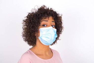 Maskeli genç bir kadın beyaz arka planda izole edilmiş. Bulaşıcı hastalıklara karşı koruma. Gündelik kıyafetler giymiş genç bir kadın.