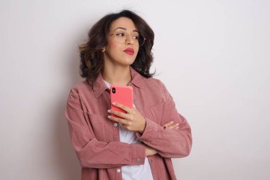 Güzel, esmer, sarışın, pembe tişörtlü, akıllı telefonlu bir kadın stüdyoya bakıyor.