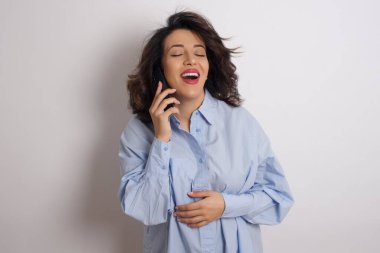 Stüdyoda mavi tişört giyen genç ve güzel bir kadın akıllı telefondan konuşuyor.