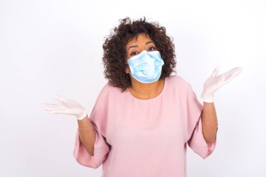 Beyaz arka planda kafası karışmış maskeli bir kadın var. Bulaşıcı hastalıklara karşı koruma. Stüdyoda poz veren günlük kıyafetler giyen genç bir kadın.