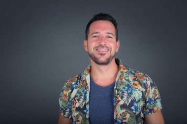 Gülümseyen ve dil gösteren neşeli yüzlü yakışıklı beyaz bir adam. Günlük giysiler giyip gri stüdyonun arka planında dikiliyorlar..