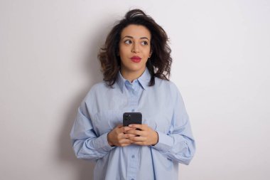 Akıllı telefonlu mavi tişörtlü genç ve güzel bir kadın stüdyoya bakıyor.