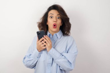 Stüdyoda kafası karışmış, mavi gömlekli, akıllı telefonlu güzel bir kadın.