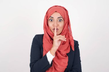 Sırrımı söyleme ya da yüksek sesle konuşma, lütfen! Duygusal olarak şaşırmış, tesettürlü Müslüman bir kadın sessiz ol der, sessiz ol der, sırlarını açığa vurmaktan korkarak, gri stüdyo duvarına karşı poz verir..