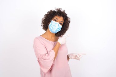 Yüzü maskeli genç bir kadın beyaz arka planda izole edilmiş. Günlük kıyafetler giymiş, yüz maskesi takan genç bir kadın. Bulaşıcı hastalıklara karşı koruma.