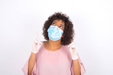 Yüzü maskeli genç bir kadın beyaz arka planda izole edilmiş. Günlük kıyafetler giymiş, yüz maskesi takan genç bir kadın. Bulaşıcı hastalıklara karşı koruma.