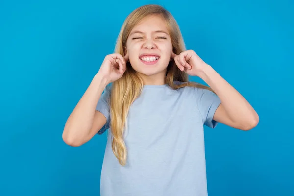 このイライラする音をやめろ 不幸なことに 青いTシャツを着た美しい白人少女が心配する顔を作り 指で耳を差し込み 大きな騒音で苛立ったことを強調しました — ストック写真