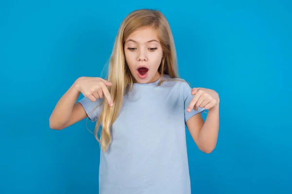 Mavi tişört giyen, ön parmaklarıyla işaret eden güzel beyaz bir kız ağzı şokla açılır. Reklam kavramı.
