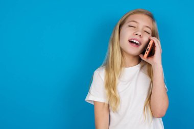 Tişört giyen güzel beyaz kız mutlu bir şekilde gülüyor, telefon görüşmesi yapıyor, arkadaşı tarafından eğlendiriliyor, gözlerini kapatıyor..