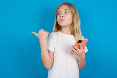  Tişört giyen güzel beyaz kız başparmağıyla işaret ediyor ve boş alan gösteriyor, cep telefonunu mesaj göndermek için tutuyor..