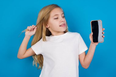 Güzel, güzel, beyaz bir kızın tişört giydiği fotoğraf. Telefon ekranı saç kuyruğu olduğunu gösteriyor.