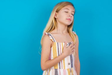 Tatmin olmuş, gülümseyen beyaz, yaz elbisesi giyen güzel bir kız ellerini karnının üstüne koyuyor. Lezzetli bir yemek yedikten sonra iyi bir ruh hali içinde olması tok olduğunu gösteriyor. Midemde hoş bir his var..