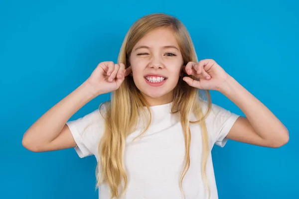 Tシャツを着ている幸せな美しい白人少女は大きな音楽を無視し 指で耳をプラグして音をオフにするように求めます — ストック写真