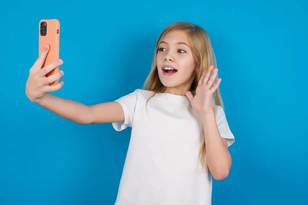 Tシャツを着ている美しい白人少女は 現代の携帯電話を保持し こんにちはジェスチャーでビデオ通話波のパームを作ります 現代テクノロジーコンセプト — ストック写真