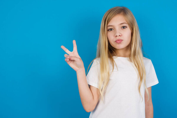  beautiful caucasian girl wearing t-shirt  makes peace gesture keeps lips folded shows v sign. Body language concept