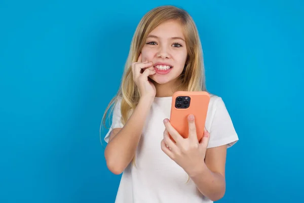 恐ろしいおかしな美しい白人少女は 電話を保持し 爪を噛むTシャツを着用しています — ストック写真