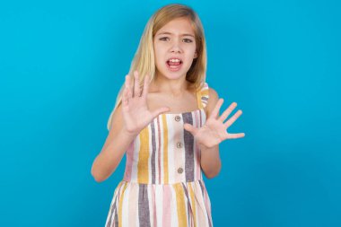 Dissatisfied beautiful caucasian girl wearing dress   frowns face, has disgusting expression, shows tongue, expresses non compliance, irritated with somebody. clipart
