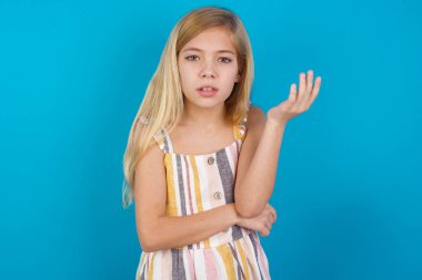 Studio shot of frustrated beautiful caucasian girl wearing dress   gesturing with raised palm, frowning, being displeased and confused with dumb question.