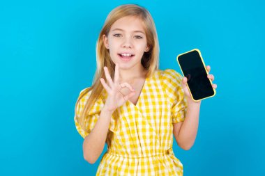 Heyecanlı beyaz kız akıllı telefon boş ekranı gösteriyor, göz kırpıyor ve el işareti yapıyor. Reklam kavramı.