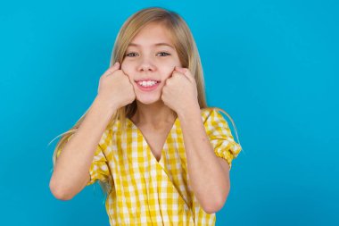 Elbise giyen güzel beyaz kız yumruklarını yanaklarında gezdiriyor. Gülümsüyor ve iyi bir ruh hali içinde olduğunu söylüyor.