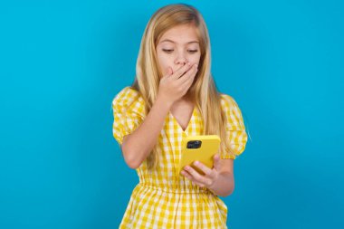 Beyaz elbiseli güzel bir kız şaşkınlığa uğruyor, akıllı telefon ekranına bakıyor, web sitesinde şok edici haberler okuyor, Omg, bu korkunç.!