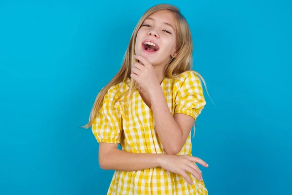 Güzel, beyaz elbiseli bir kız mutlu bir şekilde gülüyor. Elini çenesine koyuyor. Olumlu duygular ifade ediyor.