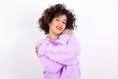 Süveter giyen hoş, genç, hoş, Latin bir kadın kendi vücudunu kucaklıyor, rahat pozlar veriyor. Şefkat ve kendine saygı kavramı