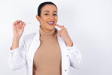  Elinde görünmez bir hizalayıcı tutan hamile bir doktor ve mükemmel düzgün dişlerini işaret ediyor. Diş sağlığı ve güven kavramı.