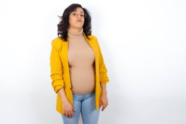 Züppe ifadeli hamile bir kadın dudaklarını kıvırıyor ve kaşlarını kaldırıyor. Şüpheli ve şüpheci bir ifadeyle bakıyor..