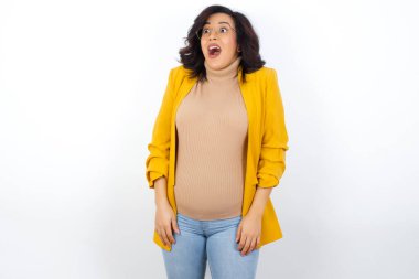 Sarı ceket giyen, omuz silken, yan bakan, mutlu ve heyecanlı hamile bir kadın. Ani tepkiler konsepti.