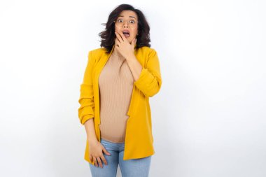 Sarı ceket giyen hamile bir iş kadını. Ağzını elleriyle kapatıyor. Bir şeyden ya da birinin çivi yemesinden korkuyor.