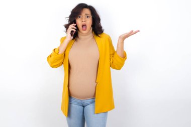   Telefonda konuşan, sarı ceketli hamile bir kadın. Utanç ve şaşkınlık dolu, sinirli ve hayal kırıklığına uğramış bir yüz. Hata için korku ve üzüntü.