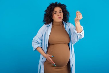 Hamile bir kadın, elinde tipik bir İtalyan jesti, kameraya bakıyor.