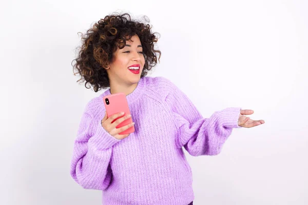 セーターを身に着けている幸せな若い美しいラテン語の女性はヤシを上げ スマートフォンはテキストメッセージやビデオ通話のための高速インターネットを使用しています — ストック写真
