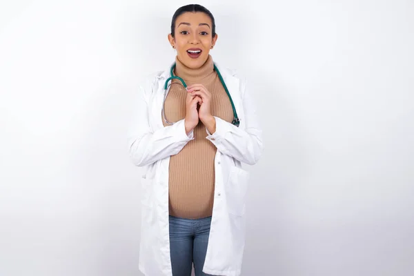 梦幻般迷人的怀孕女医生 身穿医服 面容愉悦 双手交叉 为一些令人愉快的事而兴奋 — 图库照片