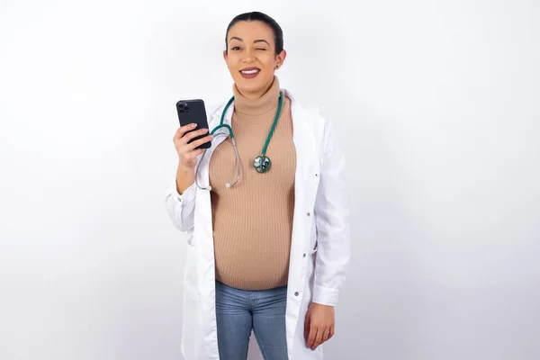 Mujer Embarazada Agradable Vistiendo Uniforme Médico Usando Teléfono Propio Mirando —  Fotos de Stock