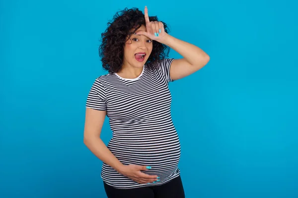 額に指でストライプTシャツのジェスチャーを身に着けている妊娠中のアラブ女性は 敗者のジェスチャーは 人々が舌を示すことを楽しませます — ストック写真